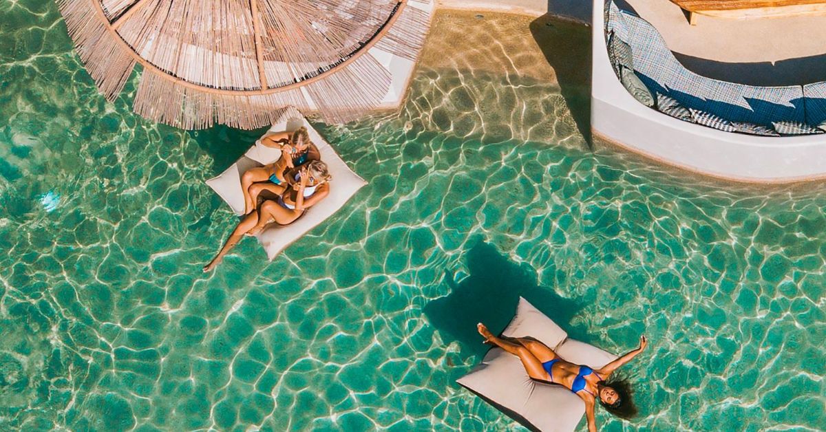 Ultra-luxury beach lifestyle in Mykonos featuring elegant sunbeds, turquoise Aegean waters, and elite travelers enjoying a refined Mediterranean summer.